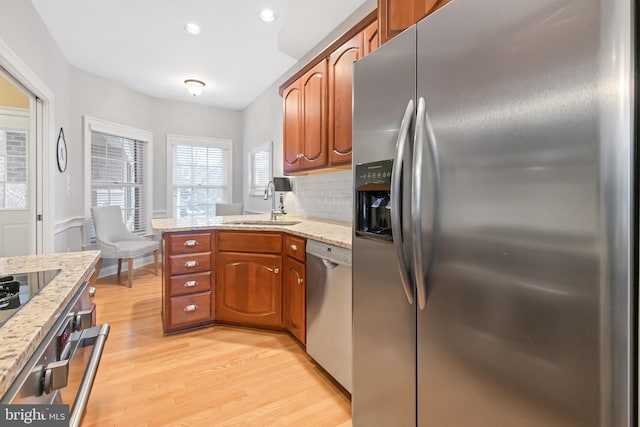 kitchen with light stone countertops, sink, stainless steel appliances, light hardwood / wood-style flooring, and backsplash