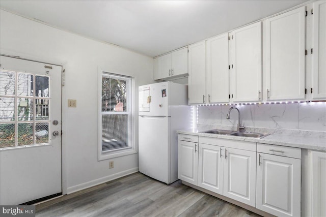 kitchen with white refrigerator, sink, light wood-type flooring, tasteful backsplash, and white cabinetry