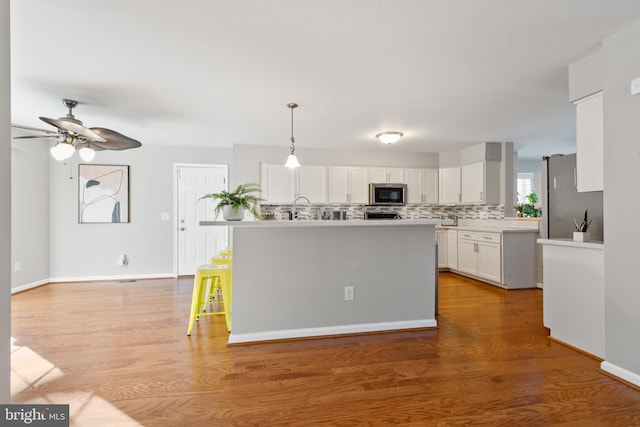 kitchen with pendant lighting, white cabinets, stainless steel appliances, and a center island with sink