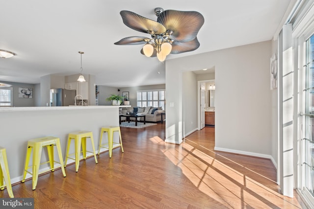 kitchen featuring a kitchen breakfast bar, sink, light hardwood / wood-style flooring, ceiling fan, and stainless steel refrigerator