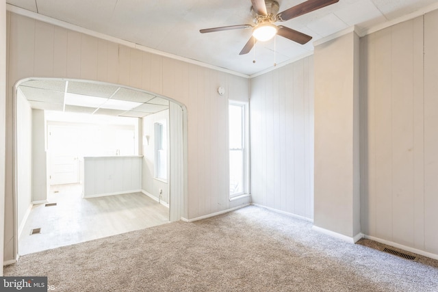 empty room featuring ceiling fan, crown molding, light carpet, and wooden walls