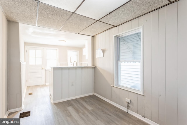 interior space featuring a drop ceiling, light hardwood / wood-style floors, sink, and wooden walls