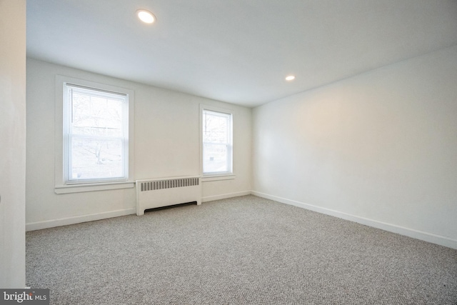 unfurnished room featuring plenty of natural light, radiator heating unit, and carpet floors