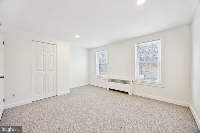 unfurnished bedroom featuring light colored carpet, radiator, and a closet