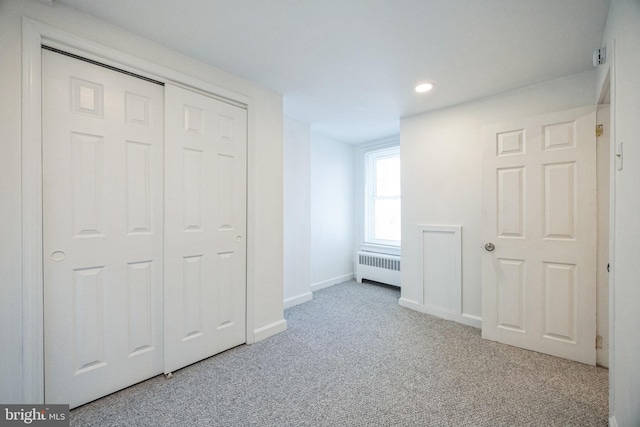 unfurnished bedroom with light colored carpet, radiator heating unit, and a closet