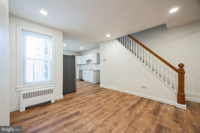 unfurnished living room with radiator, a healthy amount of sunlight, sink, and light hardwood / wood-style floors