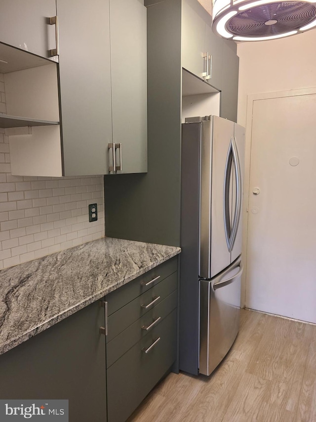 kitchen with light stone countertops, decorative backsplash, stainless steel fridge, and light hardwood / wood-style floors