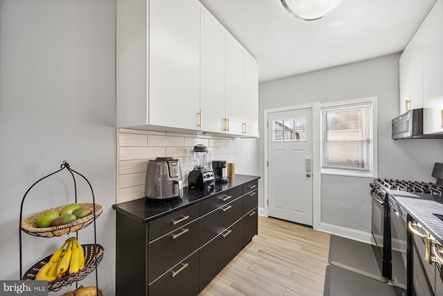 kitchen with backsplash, black range with gas stovetop, white cabinetry, and light hardwood / wood-style flooring