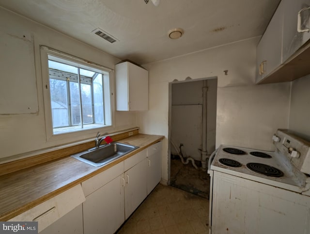 kitchen featuring electric stove, sink, and white cabinets