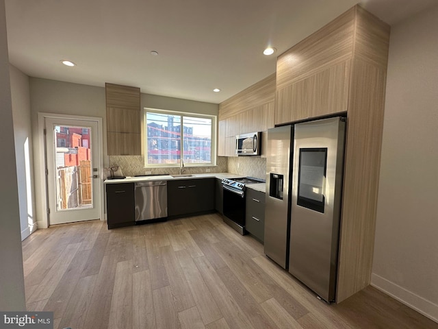 kitchen featuring decorative backsplash, appliances with stainless steel finishes, light hardwood / wood-style flooring, and sink