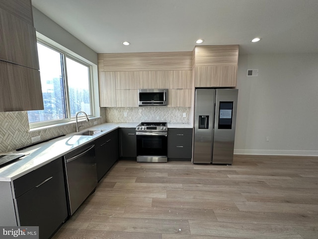 kitchen featuring appliances with stainless steel finishes, tasteful backsplash, light hardwood / wood-style flooring, and sink