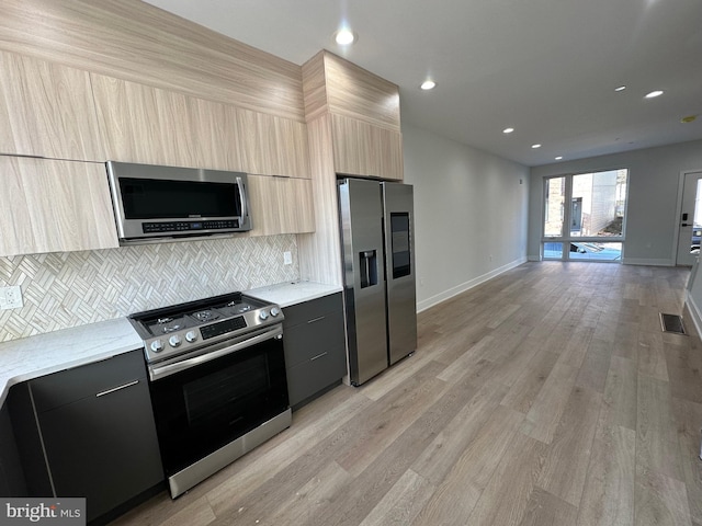 kitchen with light stone counters, light hardwood / wood-style flooring, decorative backsplash, light brown cabinetry, and appliances with stainless steel finishes