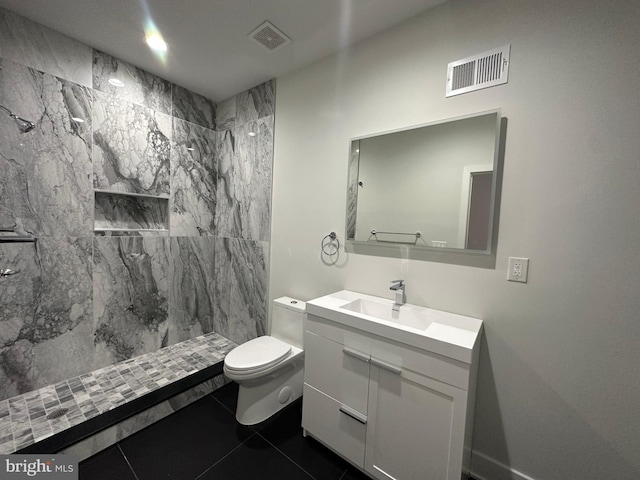 bathroom with a tile shower, tile patterned flooring, vanity, and toilet