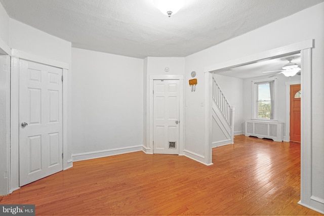 unfurnished room with ceiling fan, light hardwood / wood-style floors, radiator heating unit, and a textured ceiling