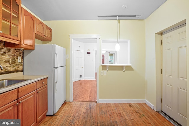 kitchen featuring decorative light fixtures, light hardwood / wood-style floors, decorative backsplash, and sink