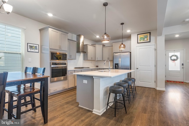 kitchen with wall chimney exhaust hood, gray cabinets, decorative light fixtures, dark hardwood / wood-style flooring, and stainless steel appliances