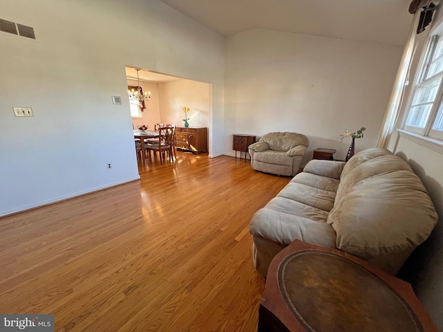 living room featuring vaulted ceiling, an inviting chandelier, and light hardwood / wood-style flooring