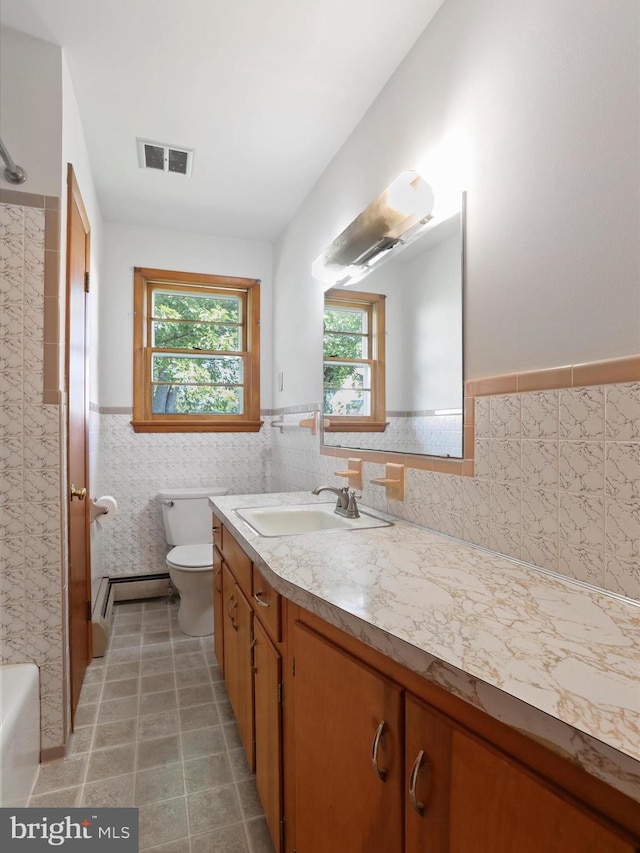 bathroom featuring a washtub, vanity, toilet, and tile walls