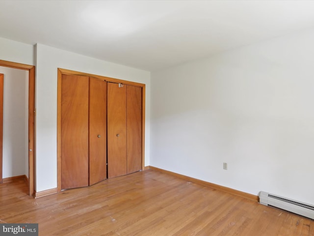 unfurnished bedroom with a closet, light hardwood / wood-style flooring, and baseboard heating