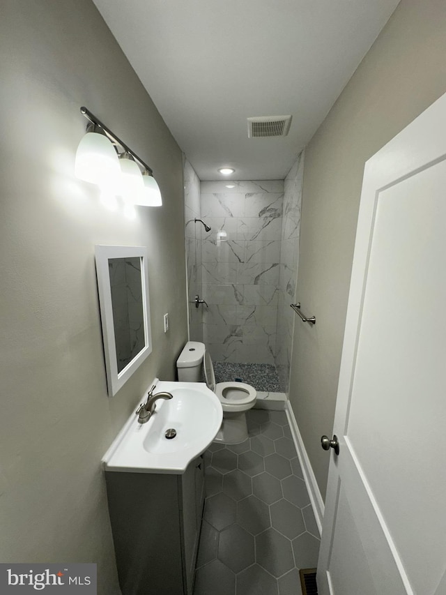 bathroom featuring vanity, a tile shower, tile patterned floors, and toilet