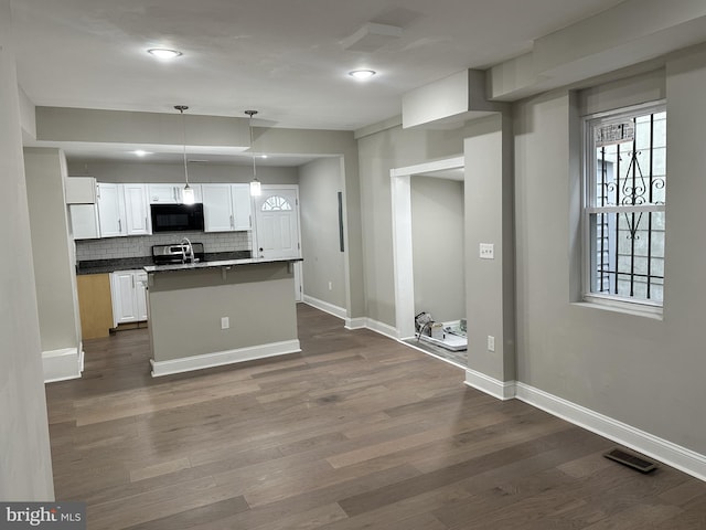 kitchen featuring white cabinetry, dark hardwood / wood-style flooring, an island with sink, pendant lighting, and decorative backsplash