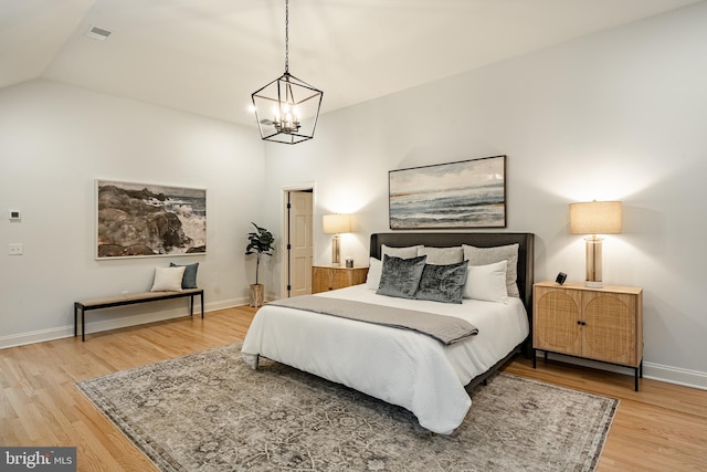 bedroom featuring hardwood / wood-style floors, vaulted ceiling, and an inviting chandelier