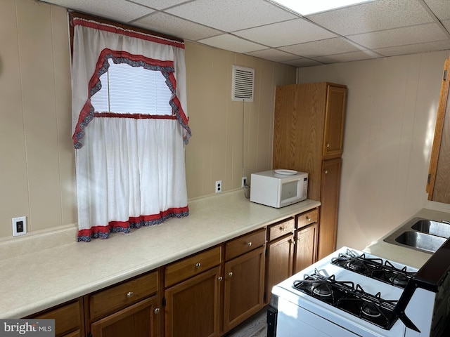 kitchen with a paneled ceiling, wooden walls, sink, and white appliances