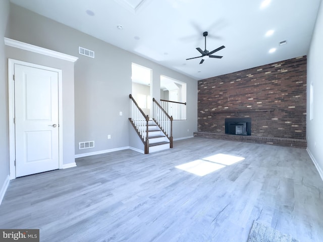 unfurnished living room with a wood stove, ceiling fan, brick wall, and hardwood / wood-style flooring