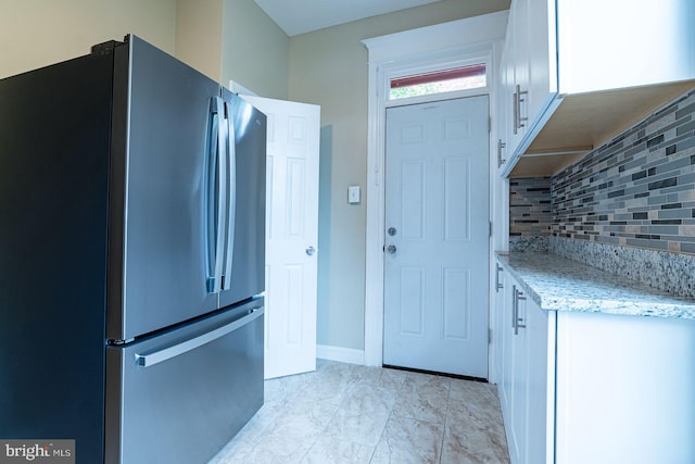 kitchen featuring decorative backsplash, stainless steel fridge, white cabinets, and light stone counters