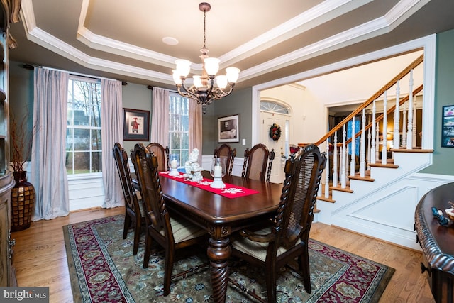 dining room featuring a tray ceiling, a chandelier, wood-type flooring, and ornamental molding