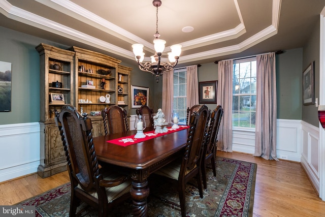 dining area featuring a chandelier, light wood-type flooring, a raised ceiling, and crown molding