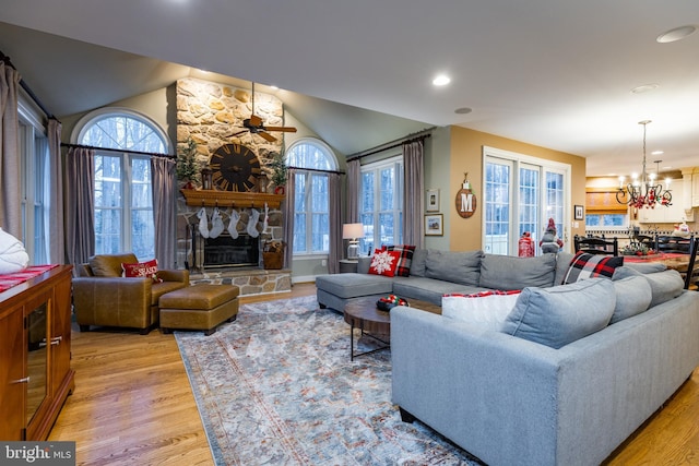 living room featuring a wealth of natural light, a stone fireplace, lofted ceiling, ceiling fan with notable chandelier, and light wood-type flooring