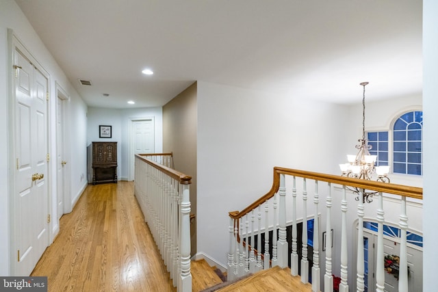 hallway with light hardwood / wood-style floors and an inviting chandelier