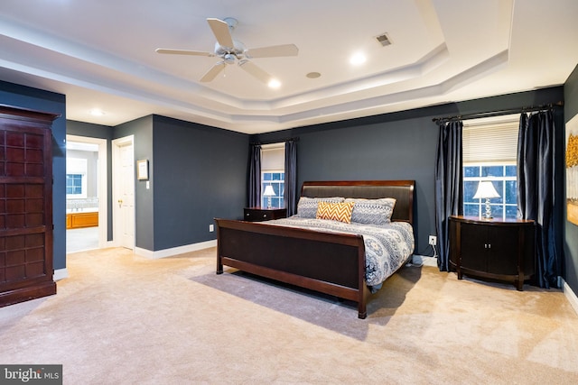 bedroom featuring light carpet, a tray ceiling, ceiling fan, and ensuite bathroom