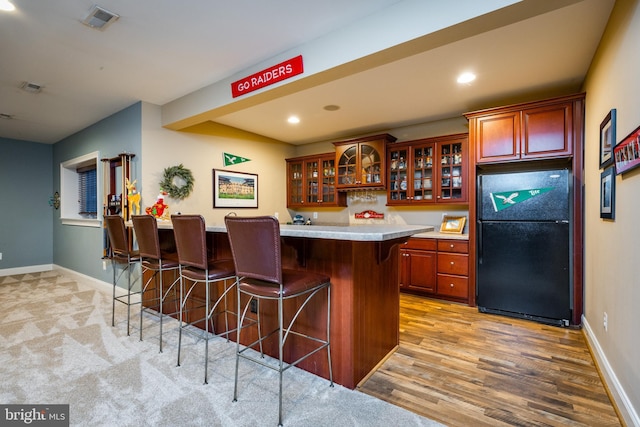 kitchen featuring a center island, black fridge, a breakfast bar area, and light hardwood / wood-style flooring