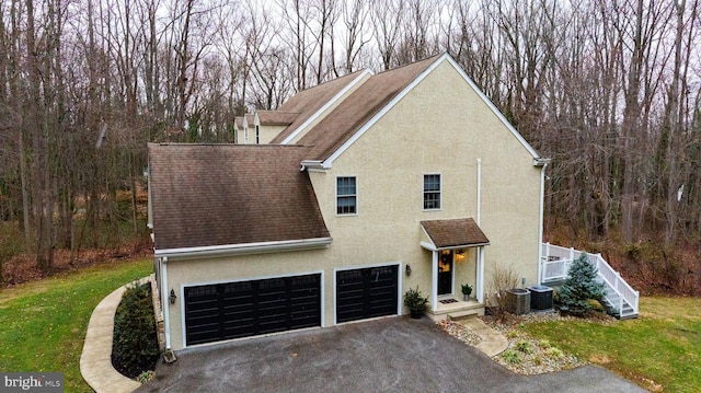 front facade featuring central AC unit, a garage, and a front lawn