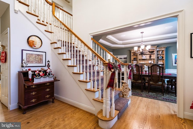 stairs with a raised ceiling, wood-type flooring, ornamental molding, and an inviting chandelier