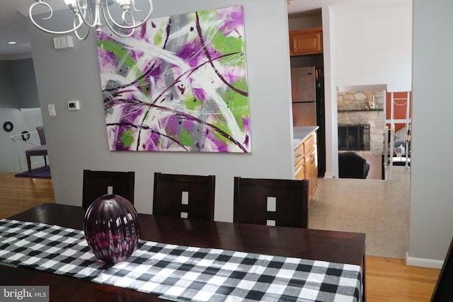 dining room featuring a stone fireplace, light wood-type flooring, and an inviting chandelier