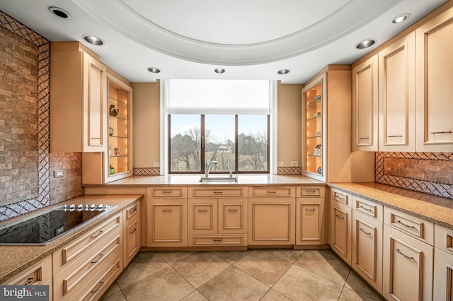 kitchen featuring black electric cooktop, light brown cabinetry, sink, and light stone countertops