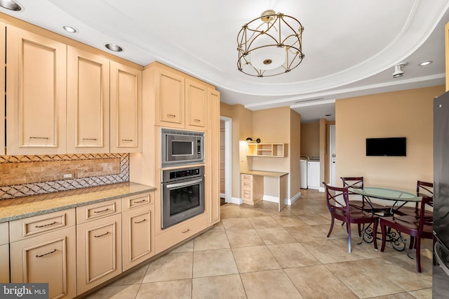 kitchen with appliances with stainless steel finishes, tasteful backsplash, light tile patterned floors, a raised ceiling, and washer and clothes dryer