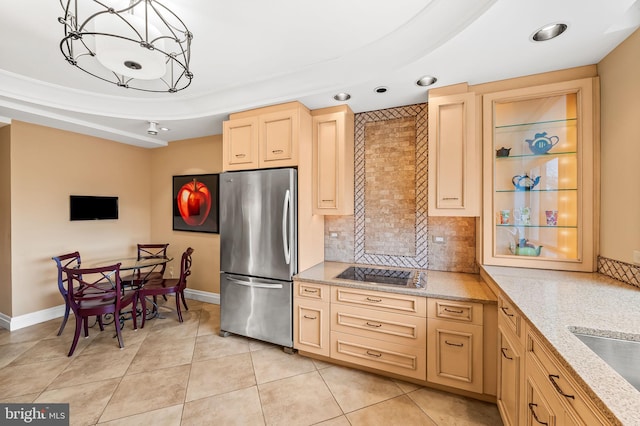 kitchen featuring light brown cabinetry, stainless steel fridge, a raised ceiling, black electric stovetop, and backsplash