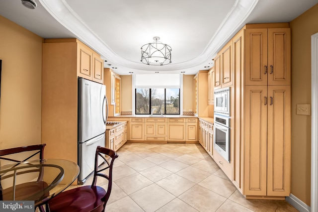 kitchen with appliances with stainless steel finishes, pendant lighting, light tile patterned floors, a raised ceiling, and light brown cabinets