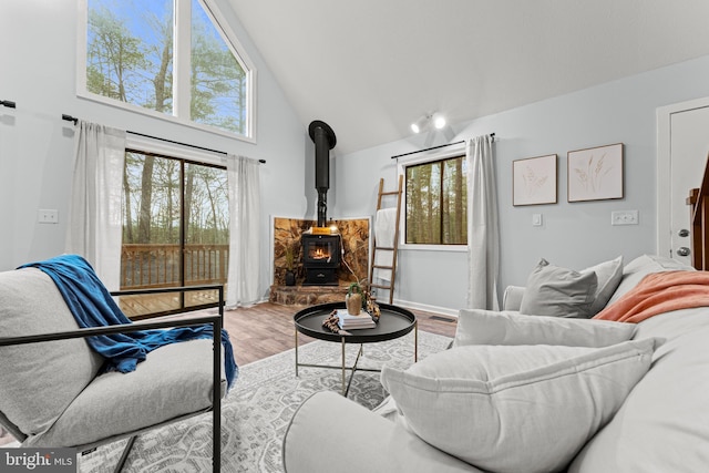 living room with light hardwood / wood-style floors, a wood stove, and high vaulted ceiling