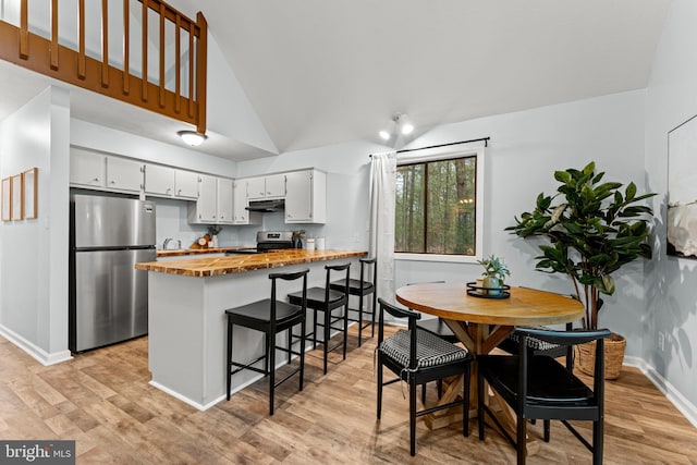 kitchen with white cabinetry, stainless steel appliances, light hardwood / wood-style flooring, lofted ceiling, and a breakfast bar area