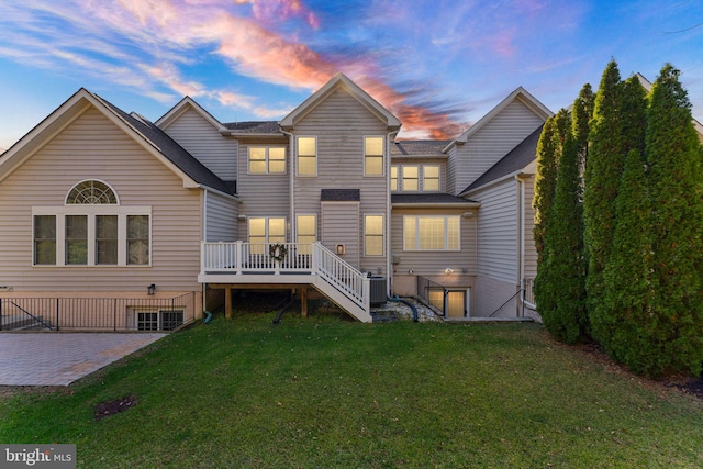 back house at dusk with central AC unit, a patio area, a lawn, and a deck