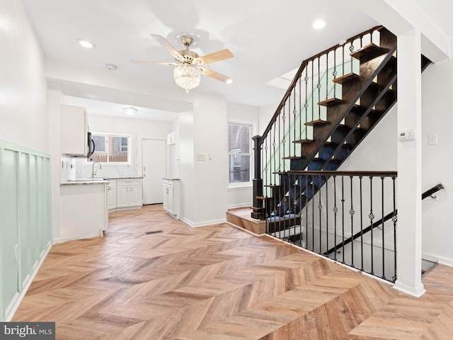 staircase with ceiling fan, a healthy amount of sunlight, and parquet flooring