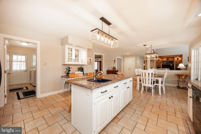 kitchen featuring a center island with sink, sink, white cabinetry, hanging light fixtures, and light stone counters