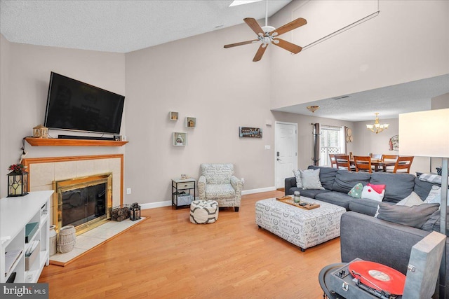 living room featuring ceiling fan with notable chandelier, vaulted ceiling, a textured ceiling, a fireplace, and wood-type flooring