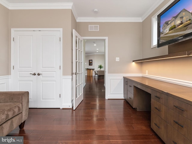 office space with visible vents, dark wood finished floors, built in desk, wainscoting, and crown molding