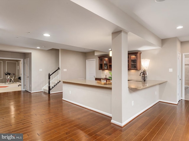 kitchen with a sink, light stone counters, tasteful backsplash, dark wood-style floors, and a peninsula